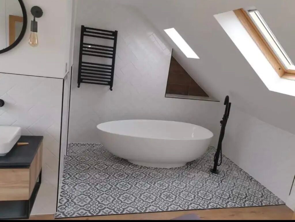 Loft conversion bathroom with a freestanding bath beneath a Velux window and patterned floor tiles